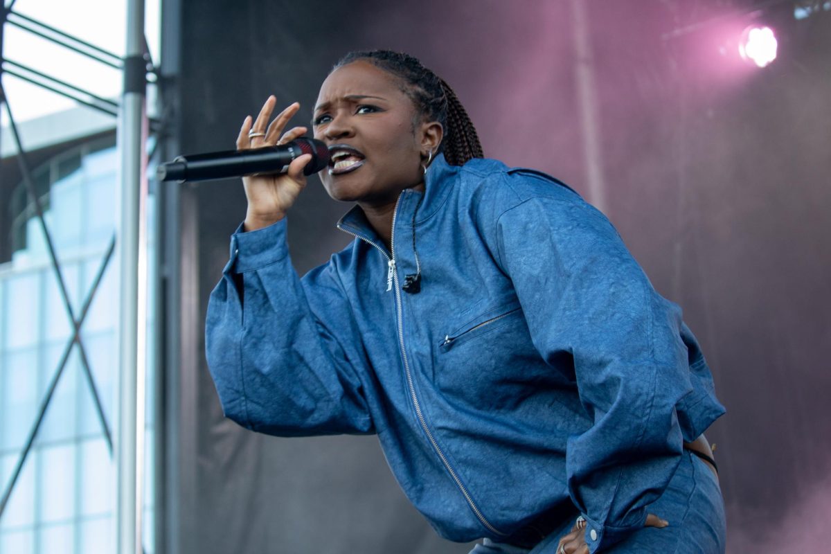 A person onstage wearing a denim jacket sings into a microphone.