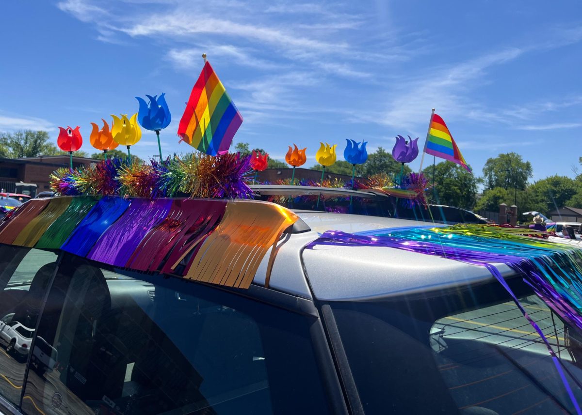 A+silver+car+decorated+with+rainbow+streamers%2C+pride+flags+and+plastic+flowers.
