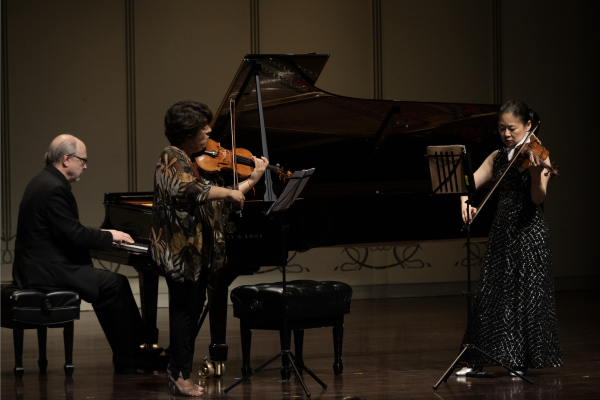 A pianist and two violinists perform on stage.