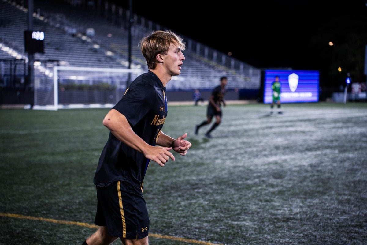 A Northwestern defender wearing a black soccer uniform with purple and gold accents surveys the field.