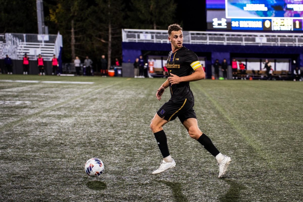 A Northwestern midfielder wearing a black soccer jersey and shorts chases the ball while scanning behind him for opponents.