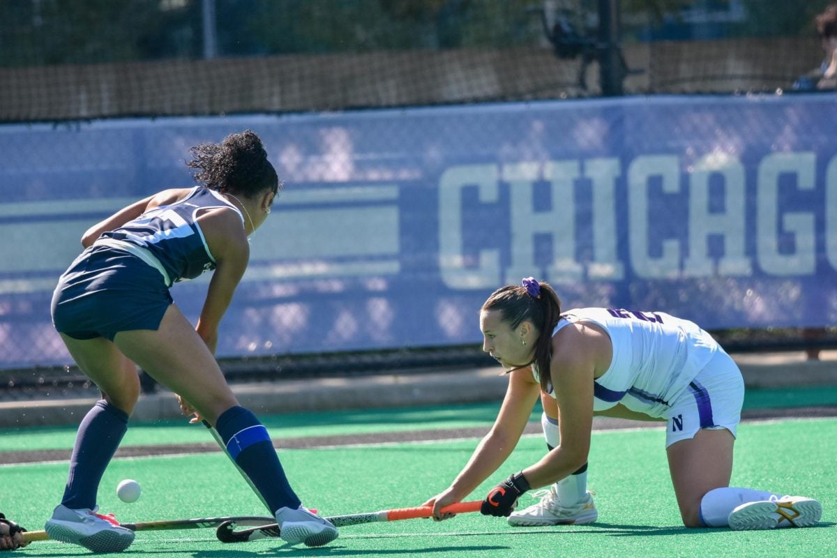 On her knee, a player holds her stick horizontally to the ground.