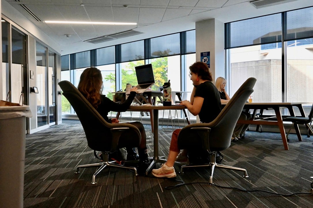 Two students sit across from each other, working on their laptops.