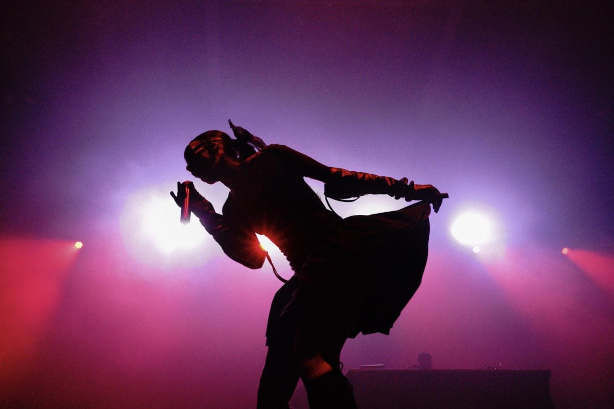 A rapper sings into a microphone as pink lights shine behind her.