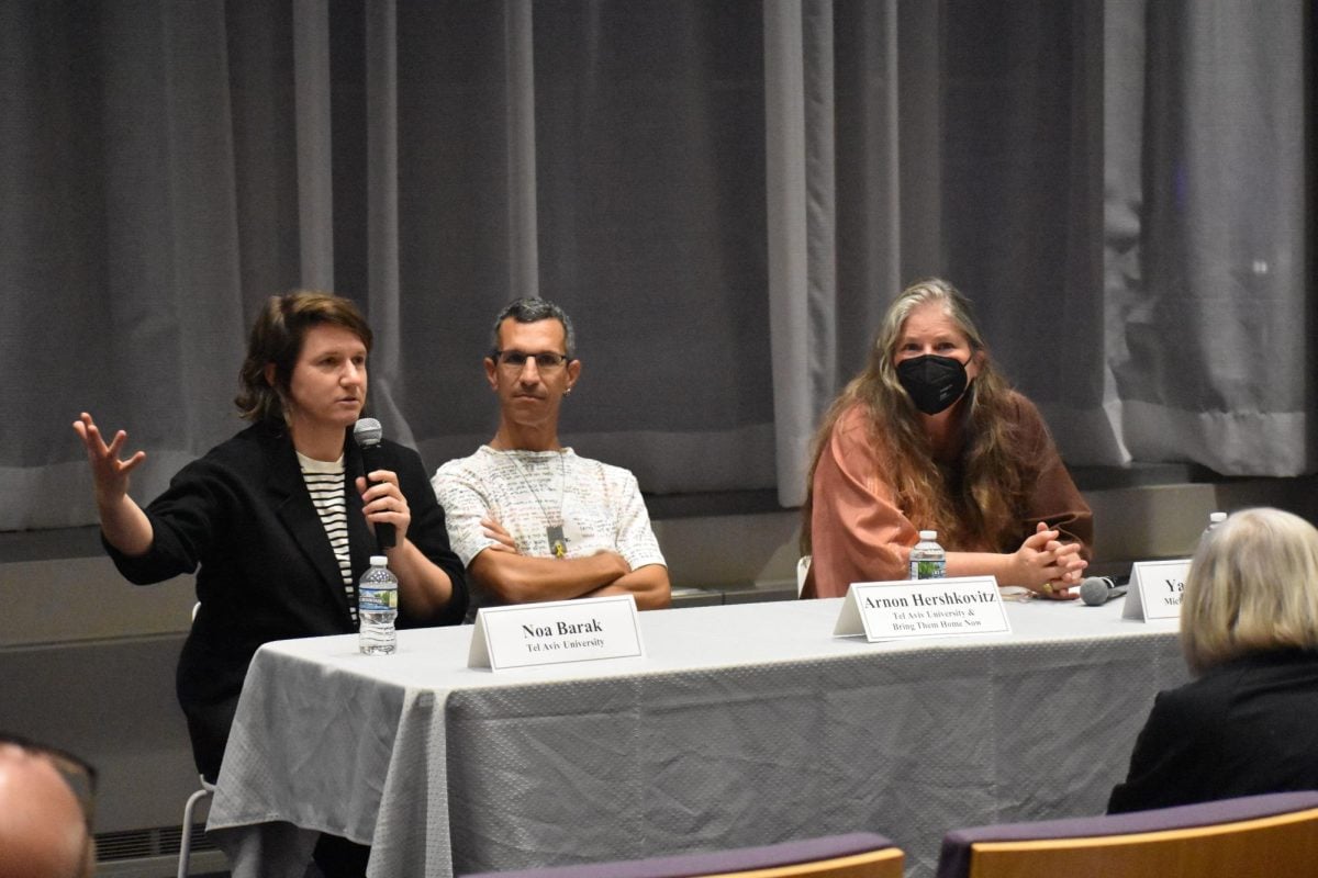 Panelists sit at a table, one speaking into a microphone while others listen.