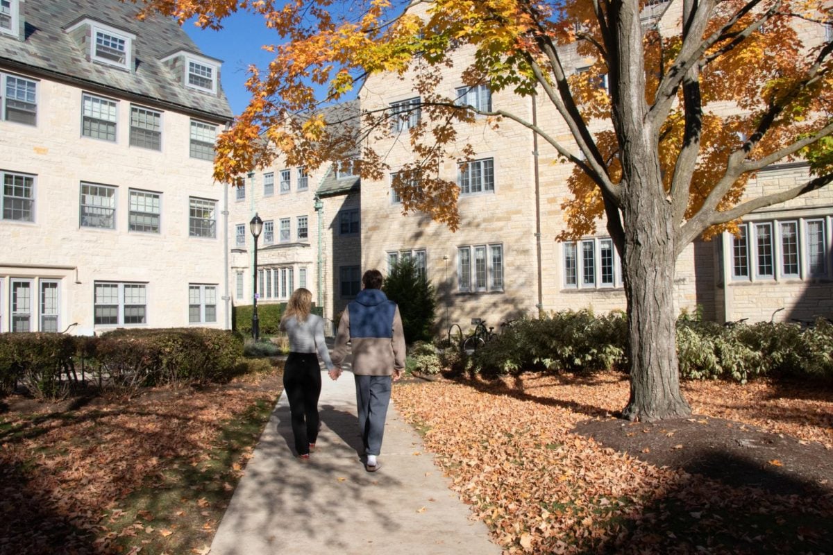 A couple walks through sorority quad holding hands next to a tree.