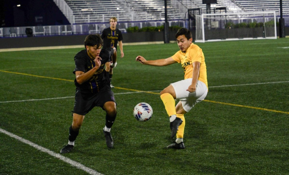 A Northwestern men’s soccer player goes for the ball against a Michigan player while another Northwestern player watches in the background.