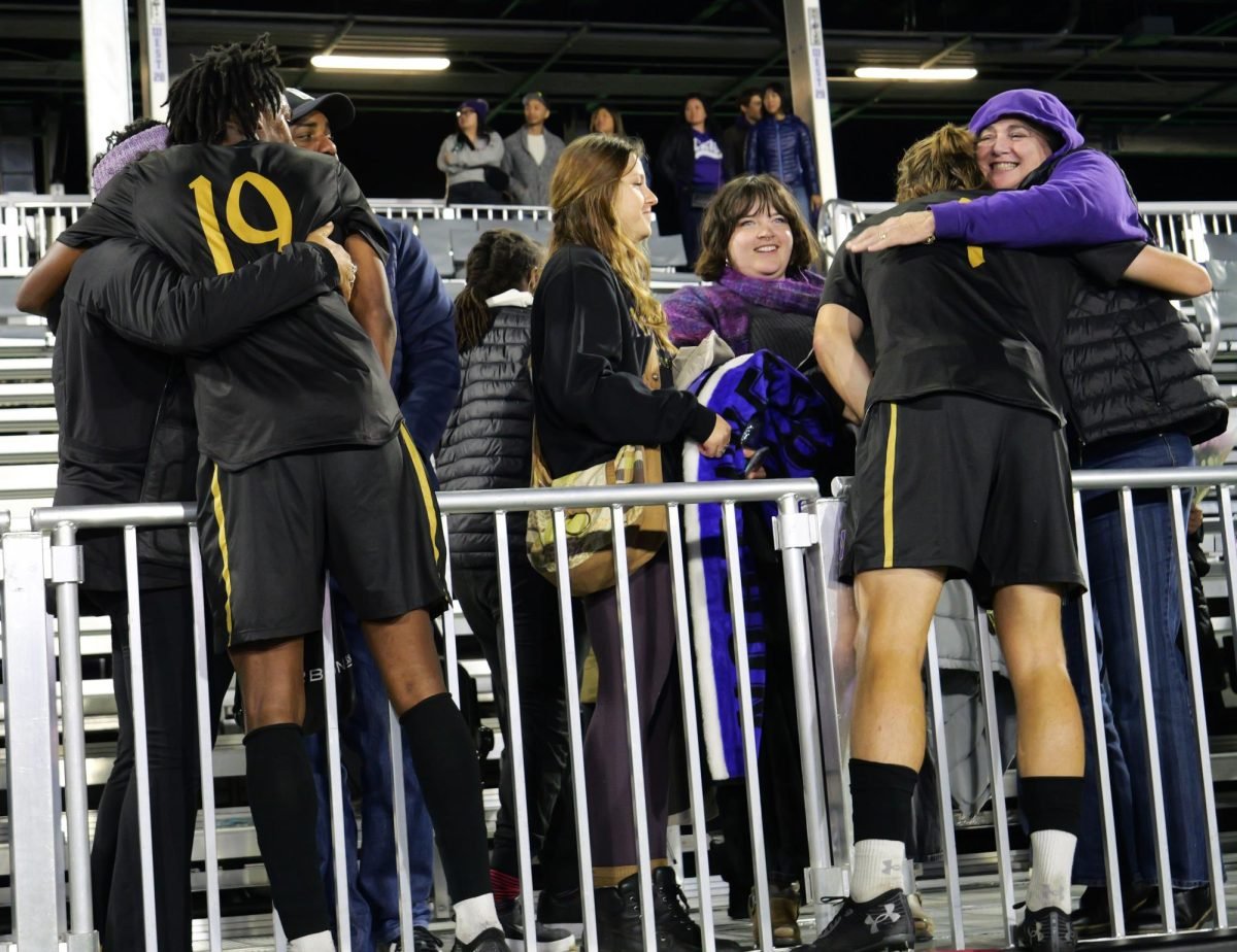 Two Northwestern players hug fans in the stands over the fence, with three other fans in between.