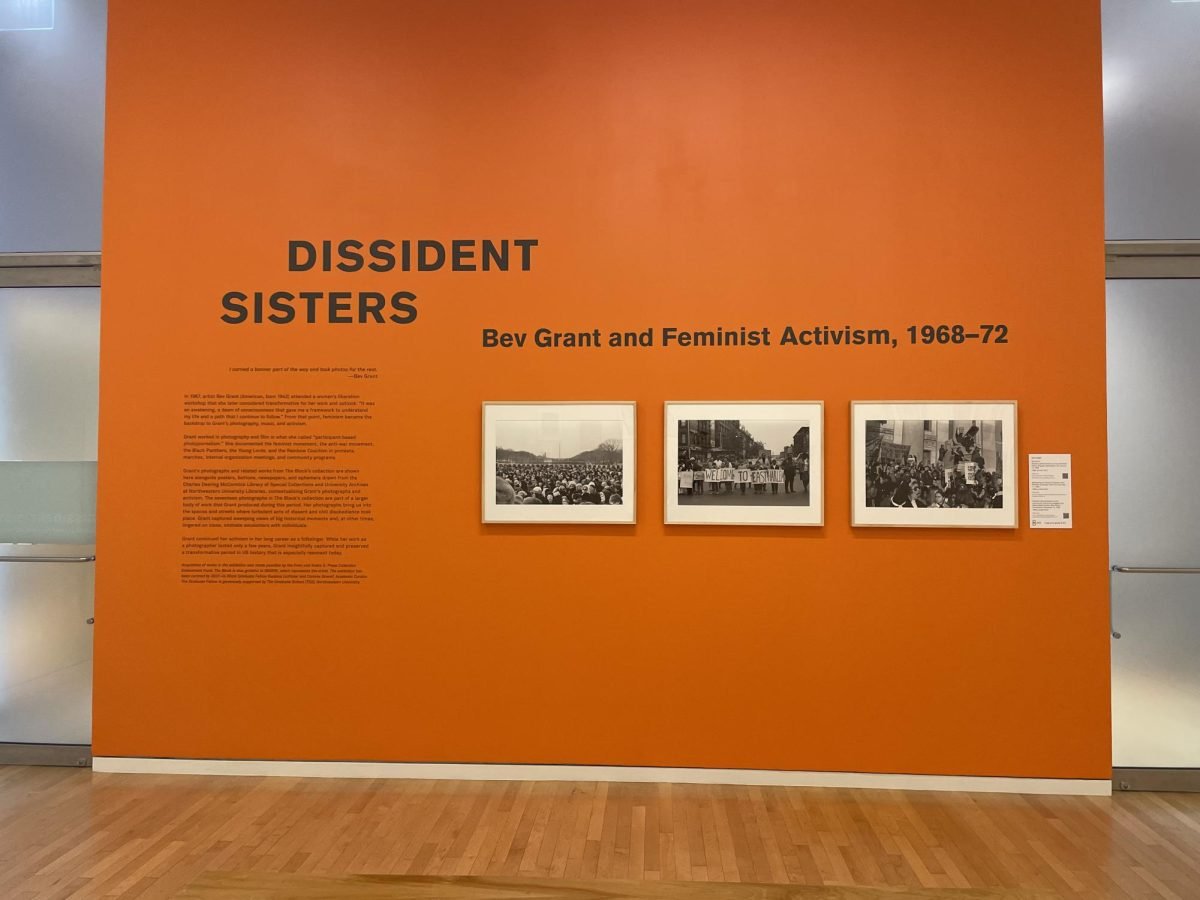 Orange wall containing explanation of “Dissident Sisters” exhibition and three black-and-white photos