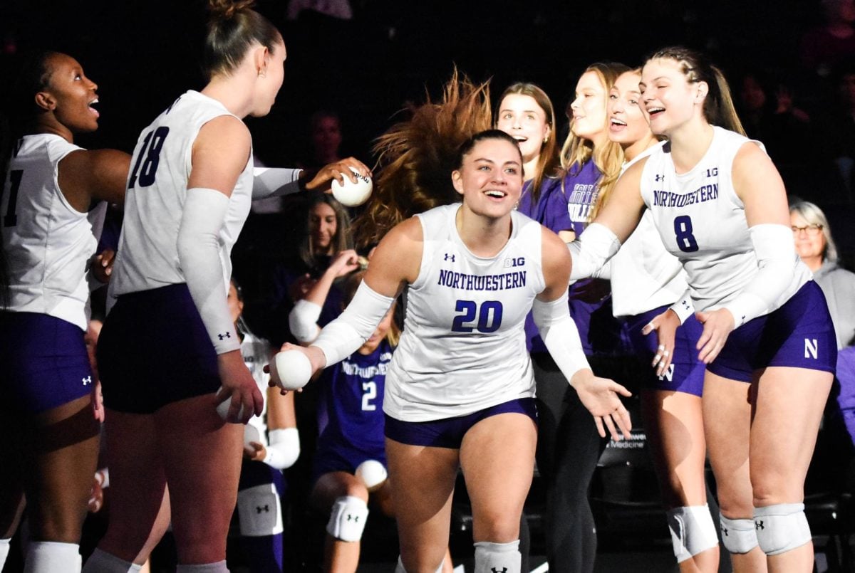 An athlete in a white jersey is welcomed onto the court by her team.