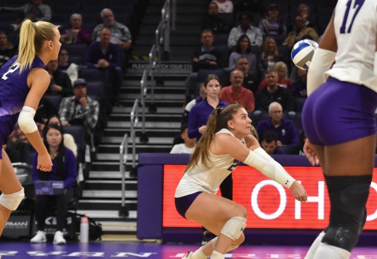 An athlete in a white jersey prepares to hit a volleyball to a teammate.