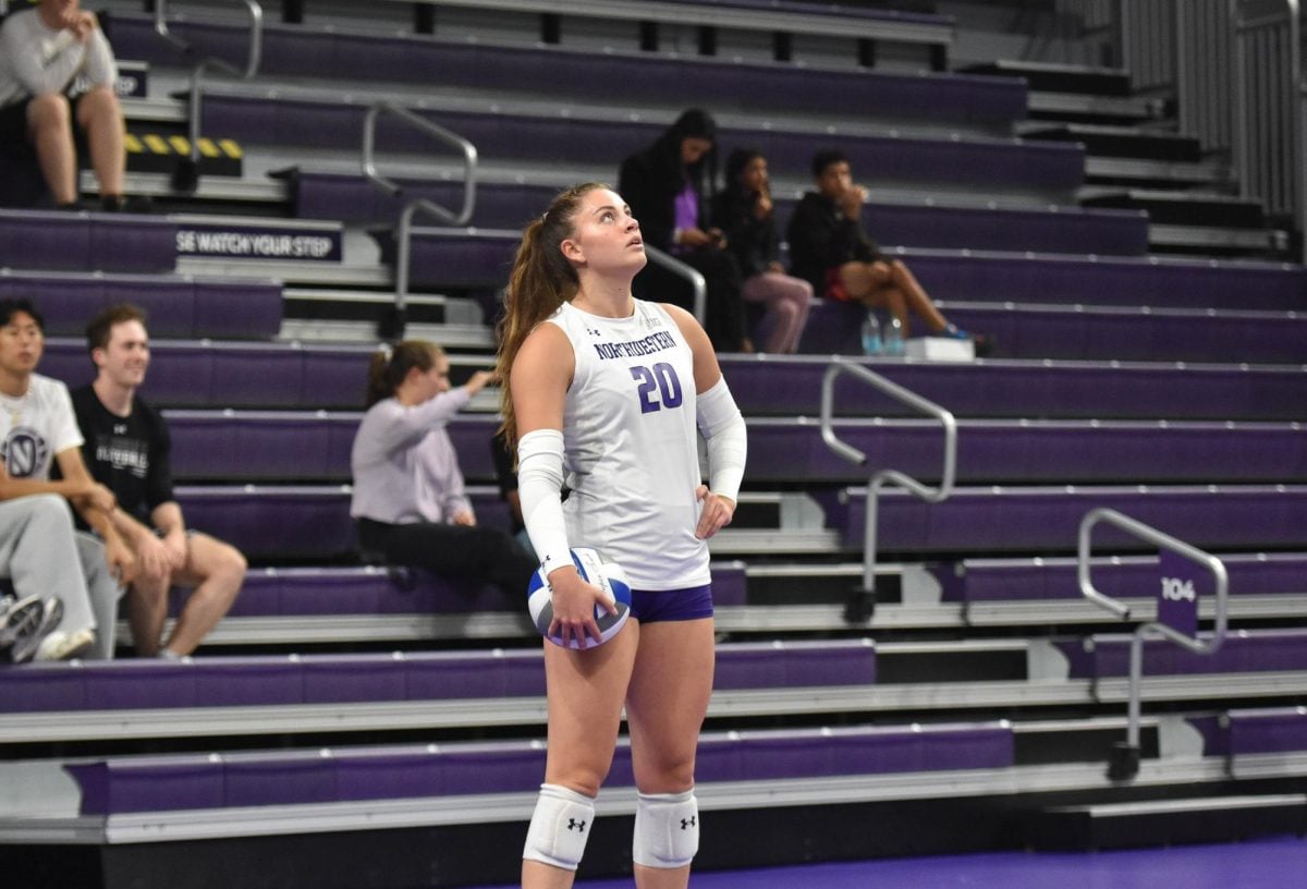 An athlete in a white jersey holds a volleyball.