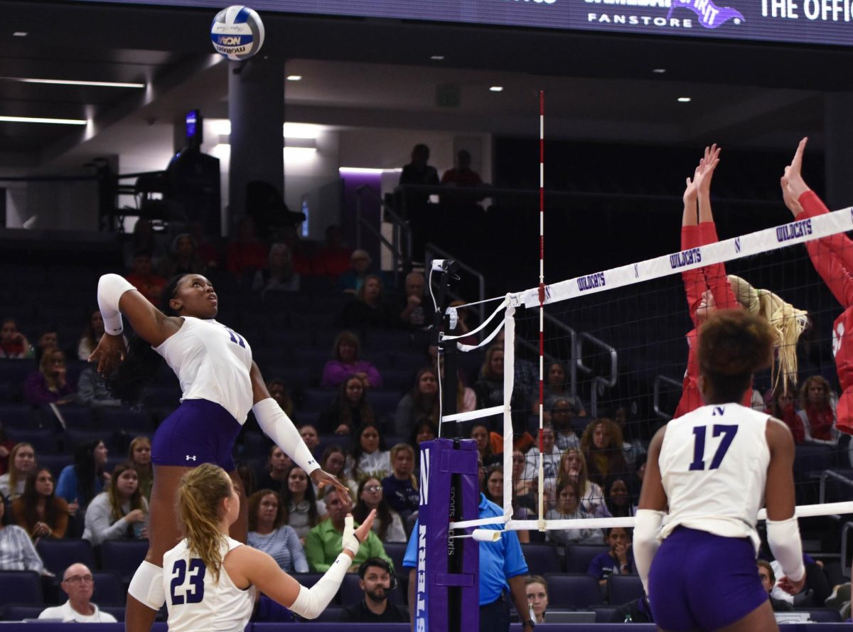 An athlete in a white jersey spikes a volleyball over a net.