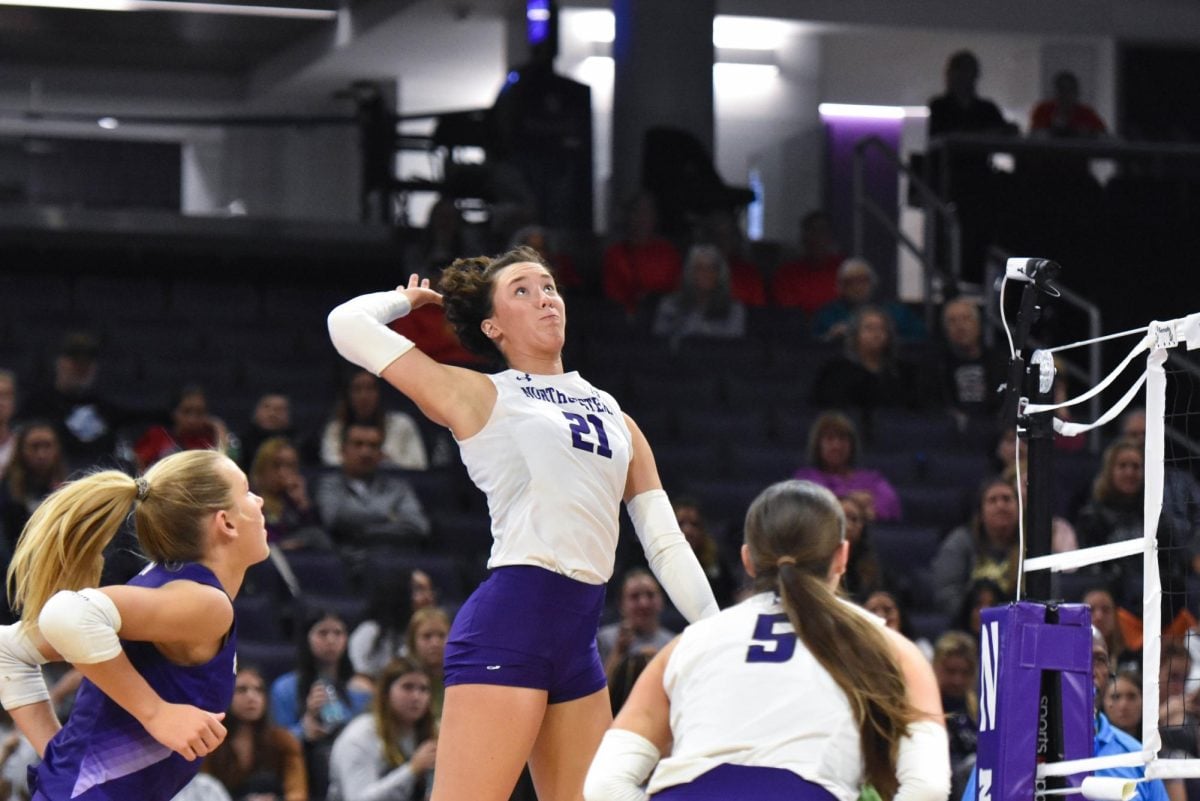 An athlete in a white jersey jumps and prepares to hit a floating volleyball.