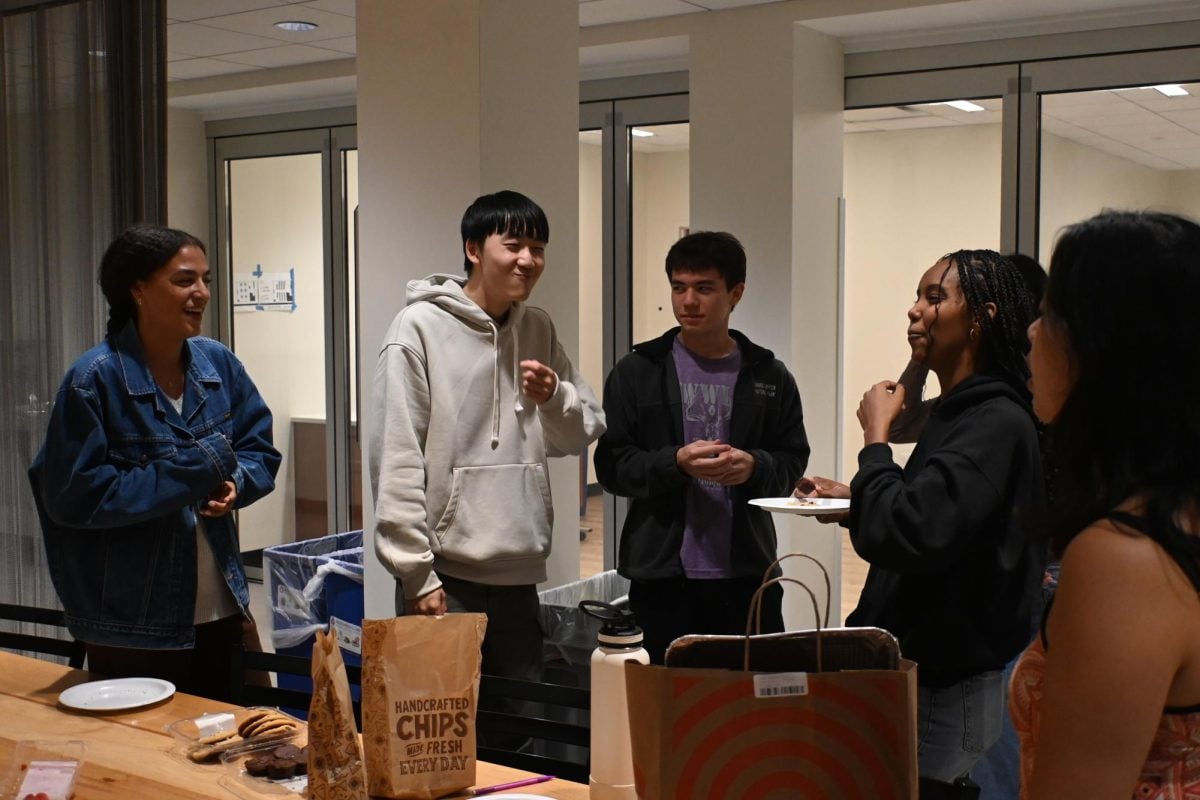 Five students crowd beside a table. They have just finished eating off their plates and are now laughing after someone has told a joke.