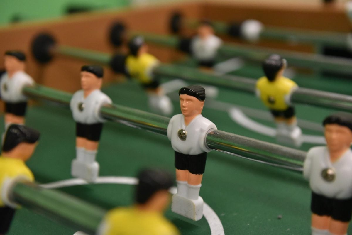 A foosball player figurine is in focus as it sits next to its row of other foosball figurines on a line that is pulled.