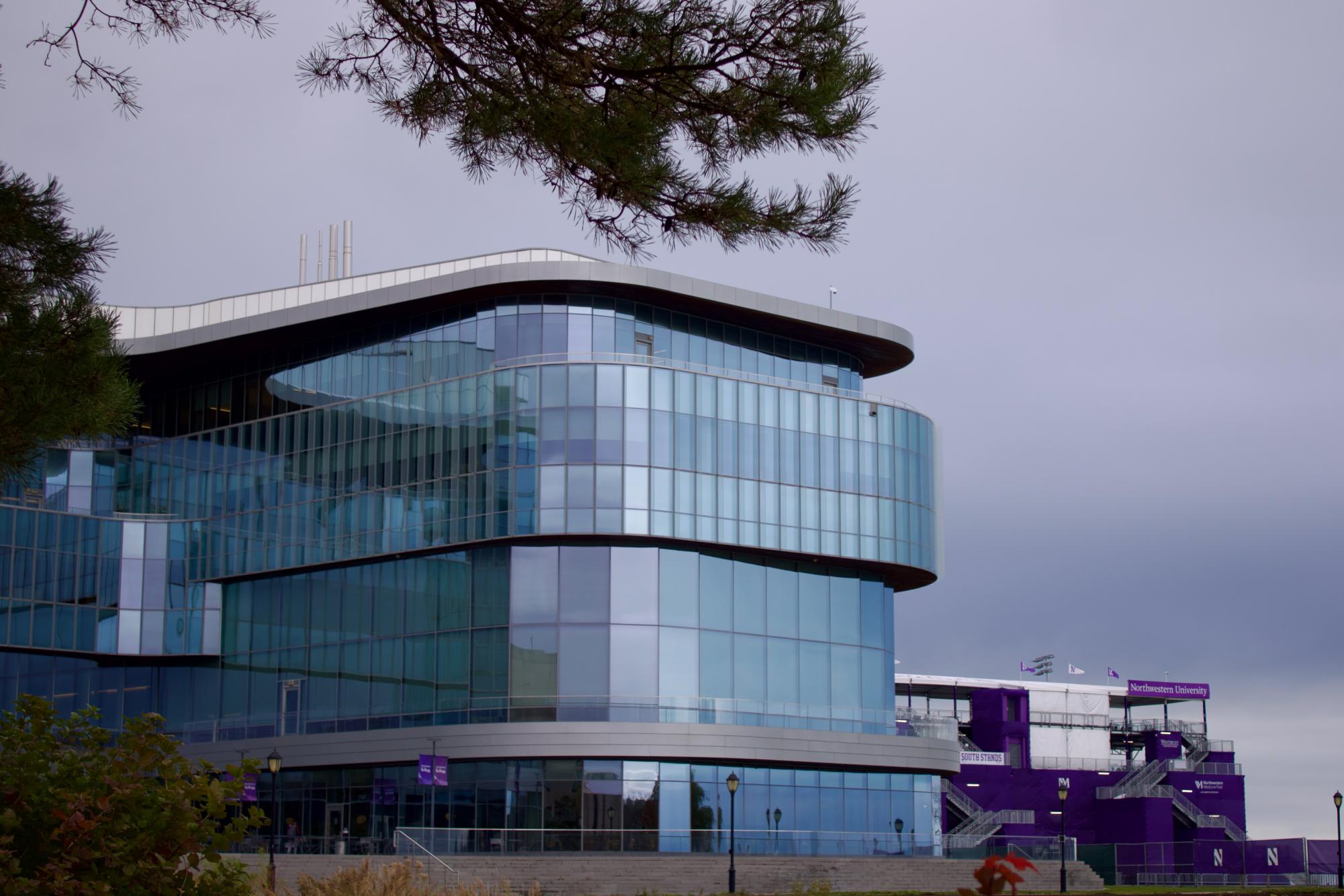 Medium shot of Kellogg exterior in front of the Lakefill with tree branches and bushes partially obstructing the view on the right.