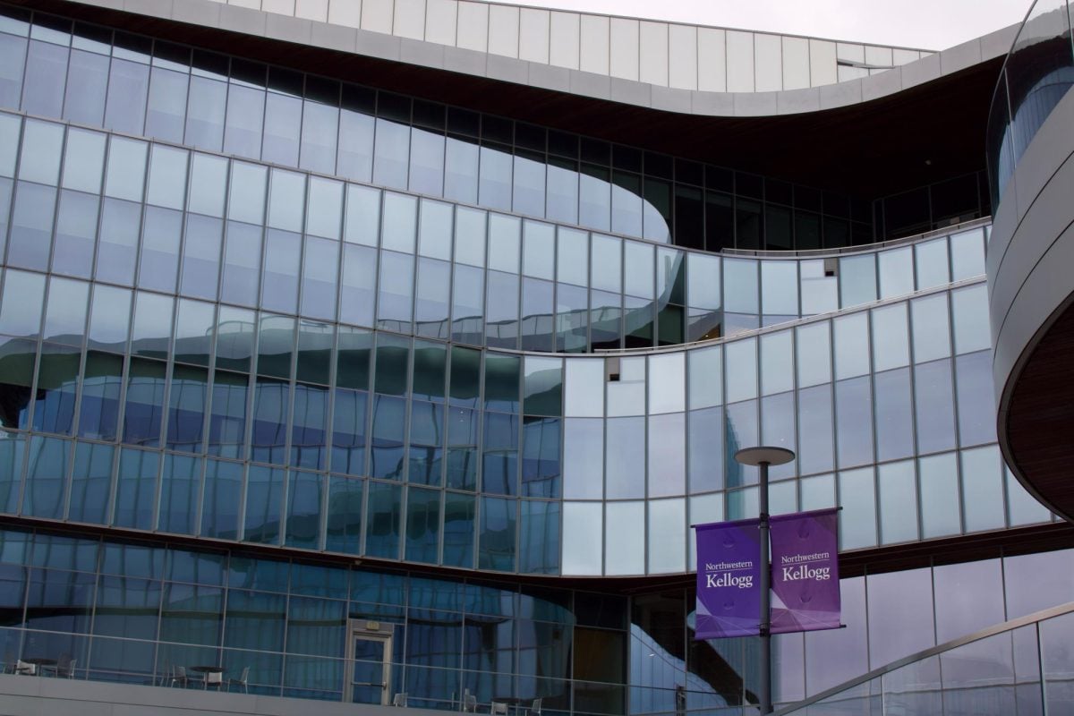 Medium, low angle shot of Kellogg’s back entrance showing open balcony area with black chairs, and two Northwestern Kellogg purple banners on the bottom right. 