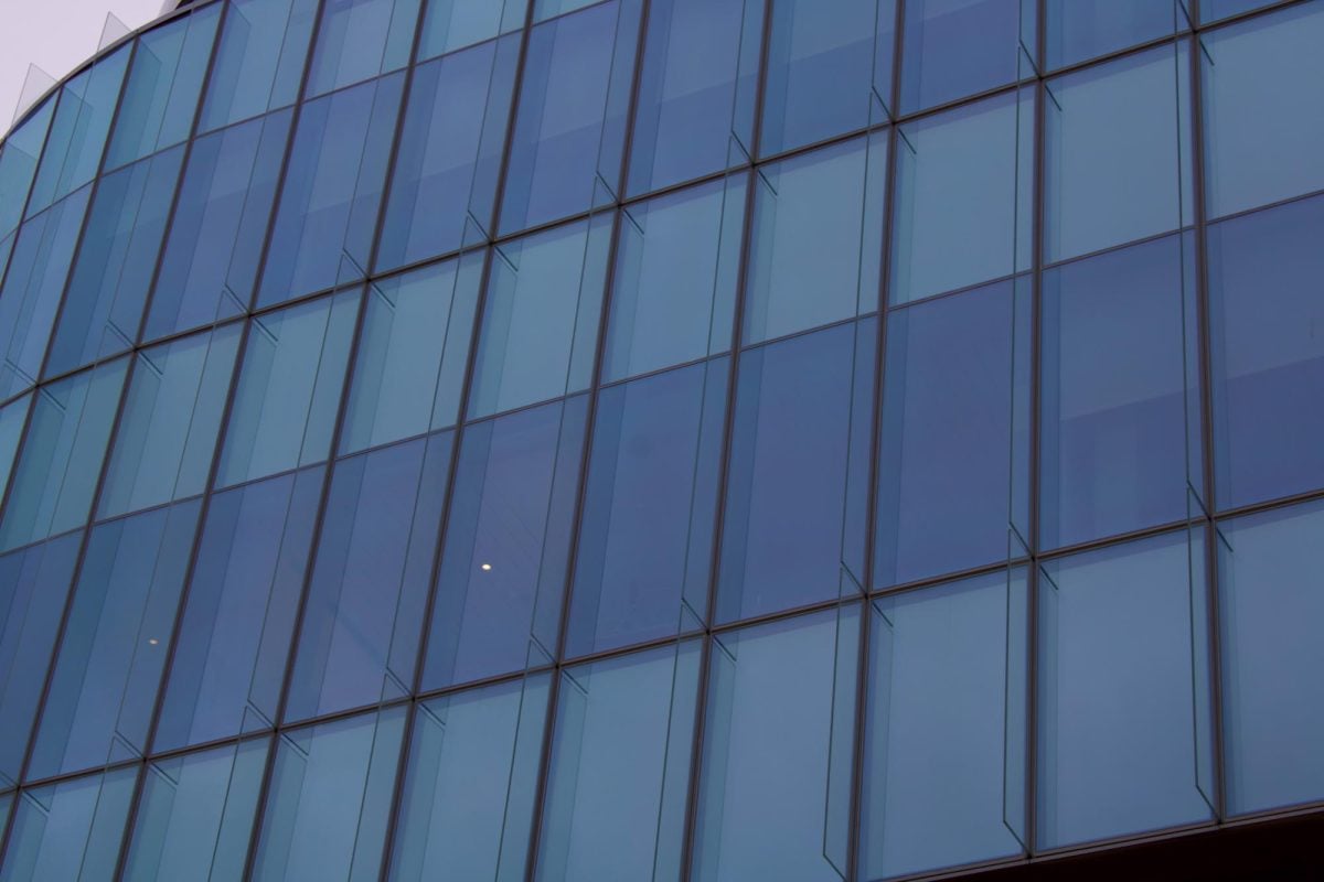 Close-up of exterior glass window pattern reflecting sky hues with semi-transparent visibility into Kellogg’s interior.