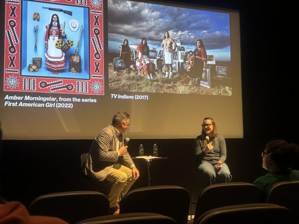 Cara Romero and Aaron Golding laugh onstage in front of two images of Romero’s photographs.