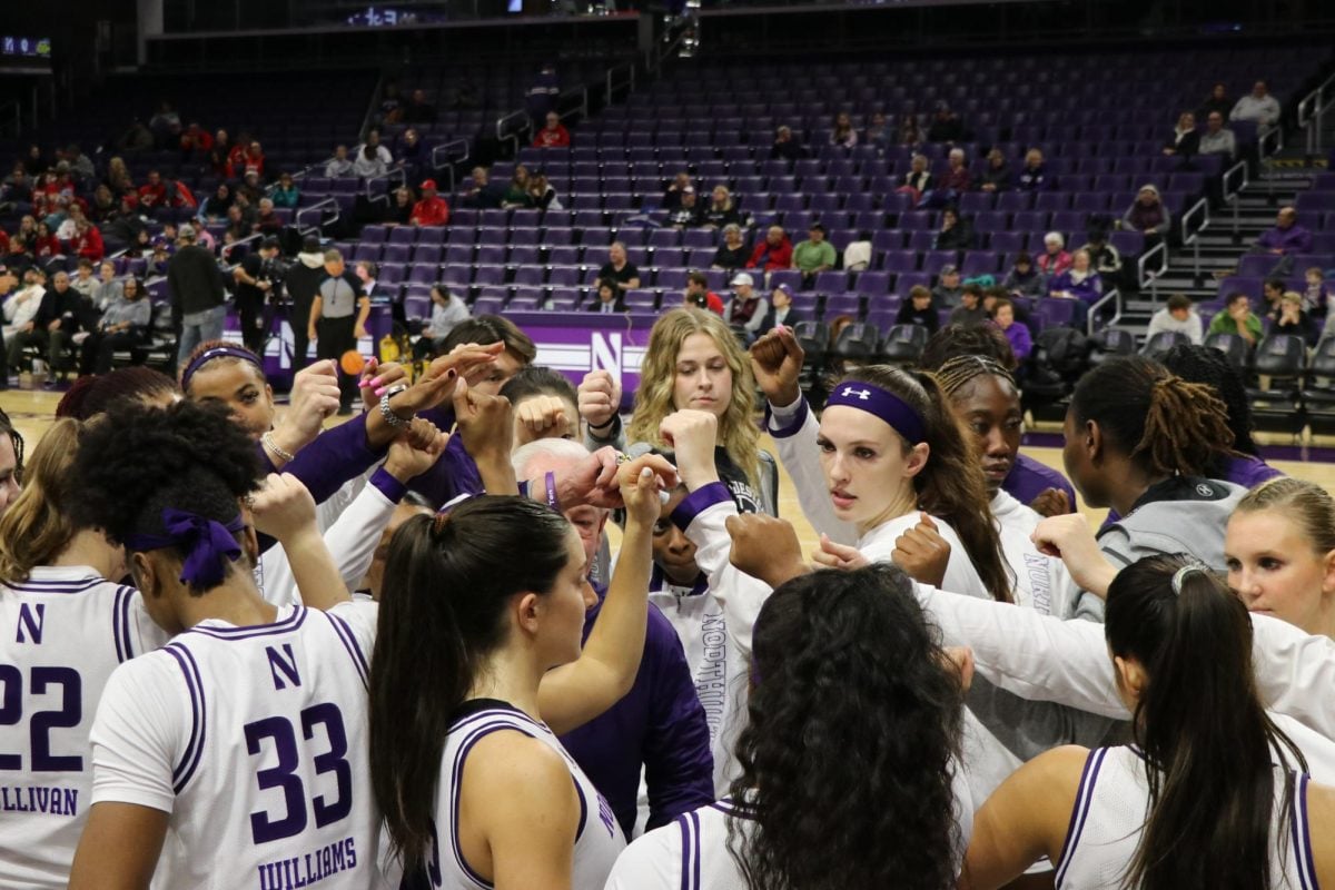 The women’s basketball team puts their fists in the air during a huddle.