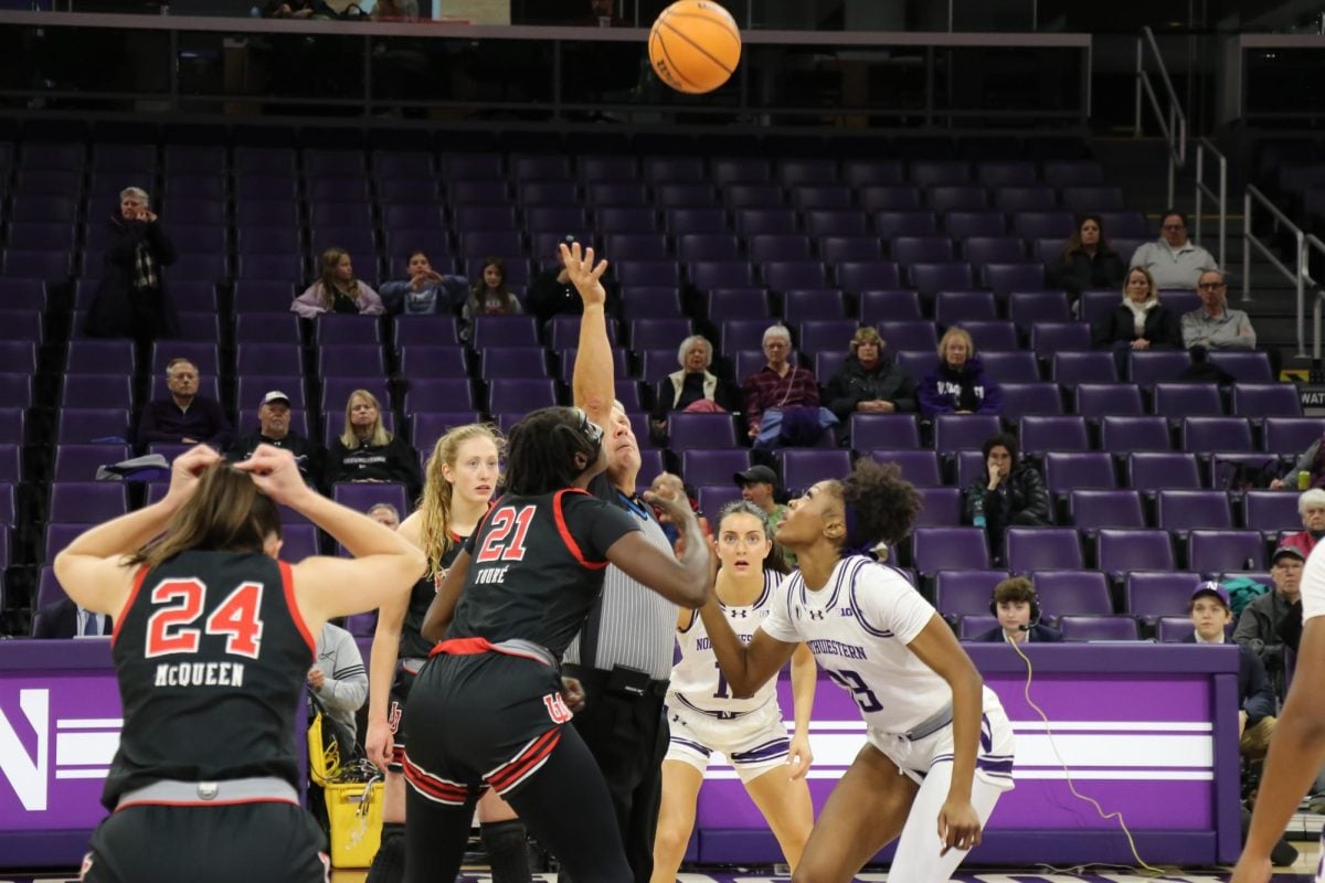 A referee throws the basketball into the air above players.