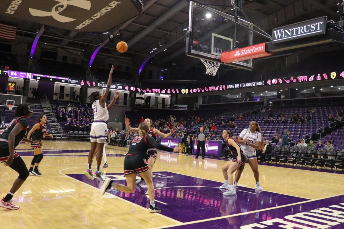 A player jumps to shoot the ball while opposing team players rush to defend her.