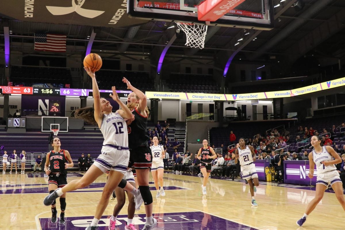 A player jumps to make a basket while being guarded by a player from the opposing team.