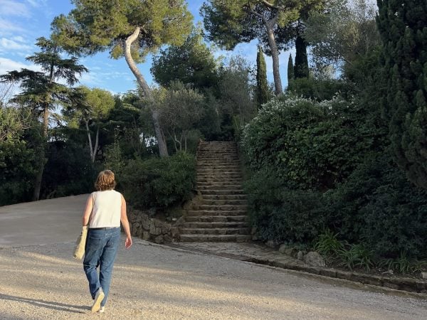 Student in white top and blue jeans walks up the road at the Parque Guëll in Barcelona on a clear day.