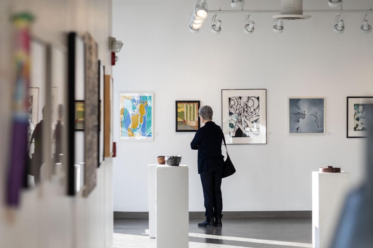 Patron looks at a wall of paintings, facing away from the camera.