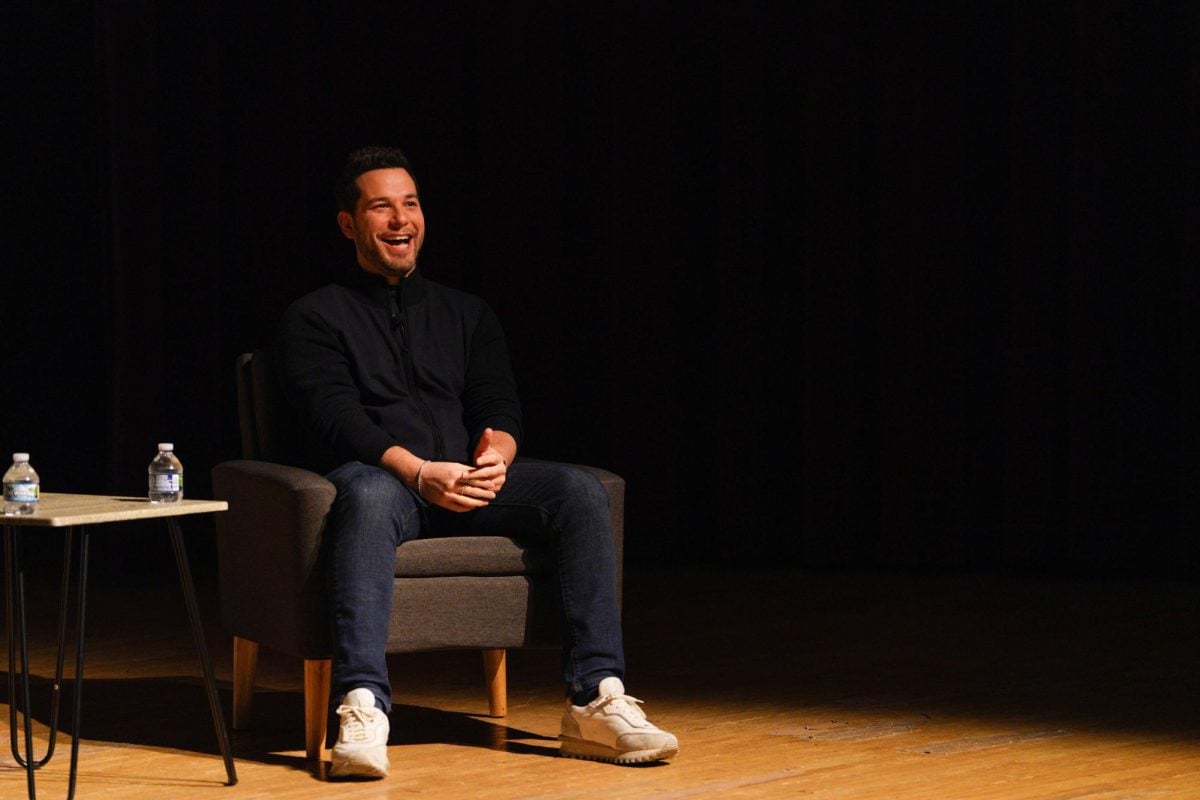 A man sits on stage laughing and looking towards the audience