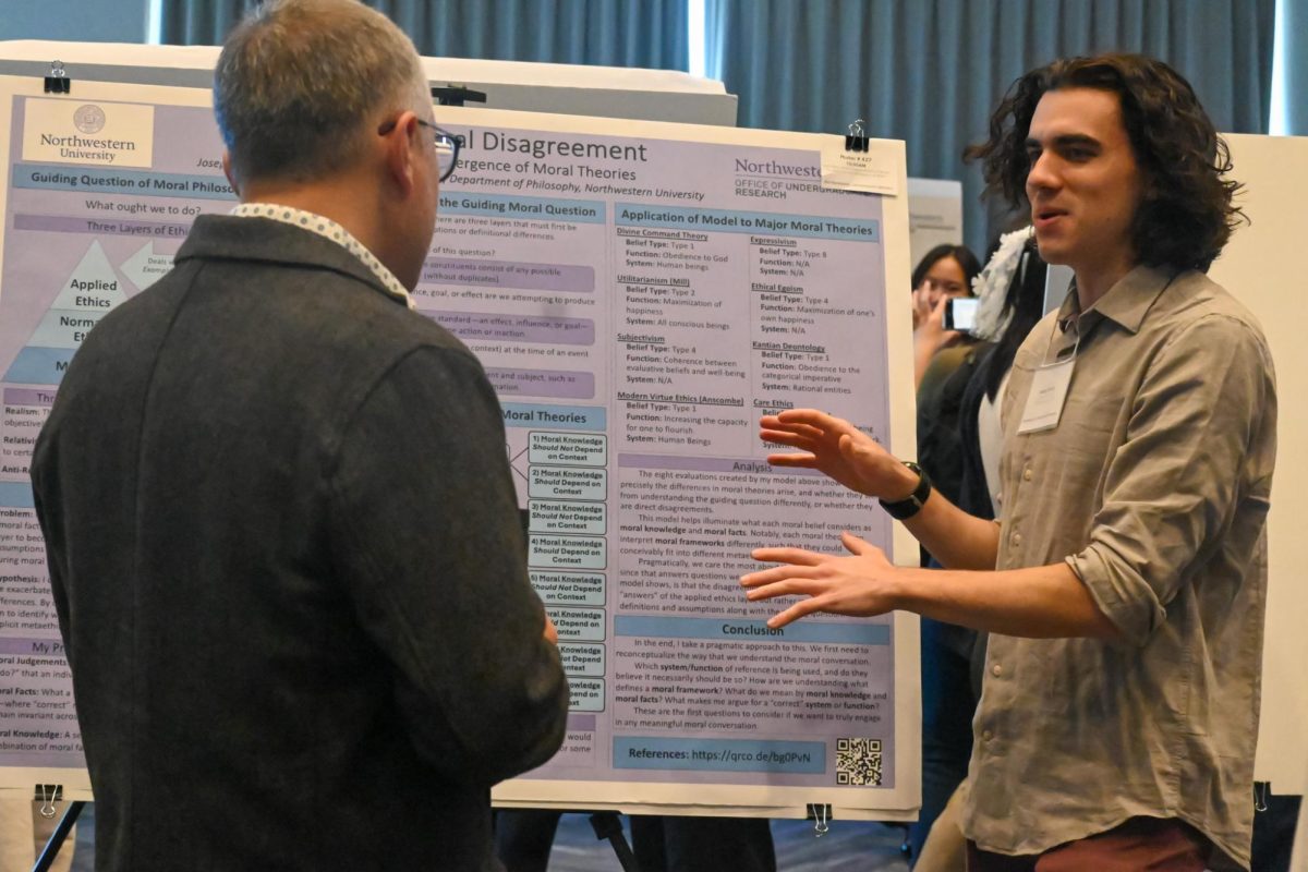 A student gestures at a posterboard while talking to an attendee.