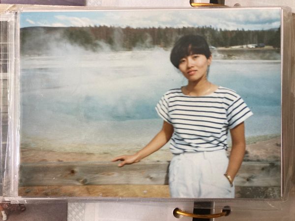 A picture of a woman standing in front of a body of water and woods. 