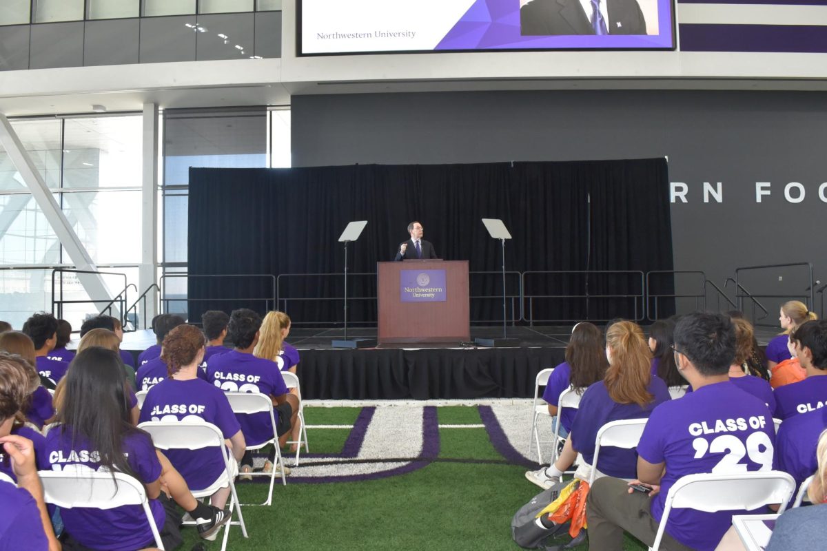 A man in a suit speaks to a large group in purple.