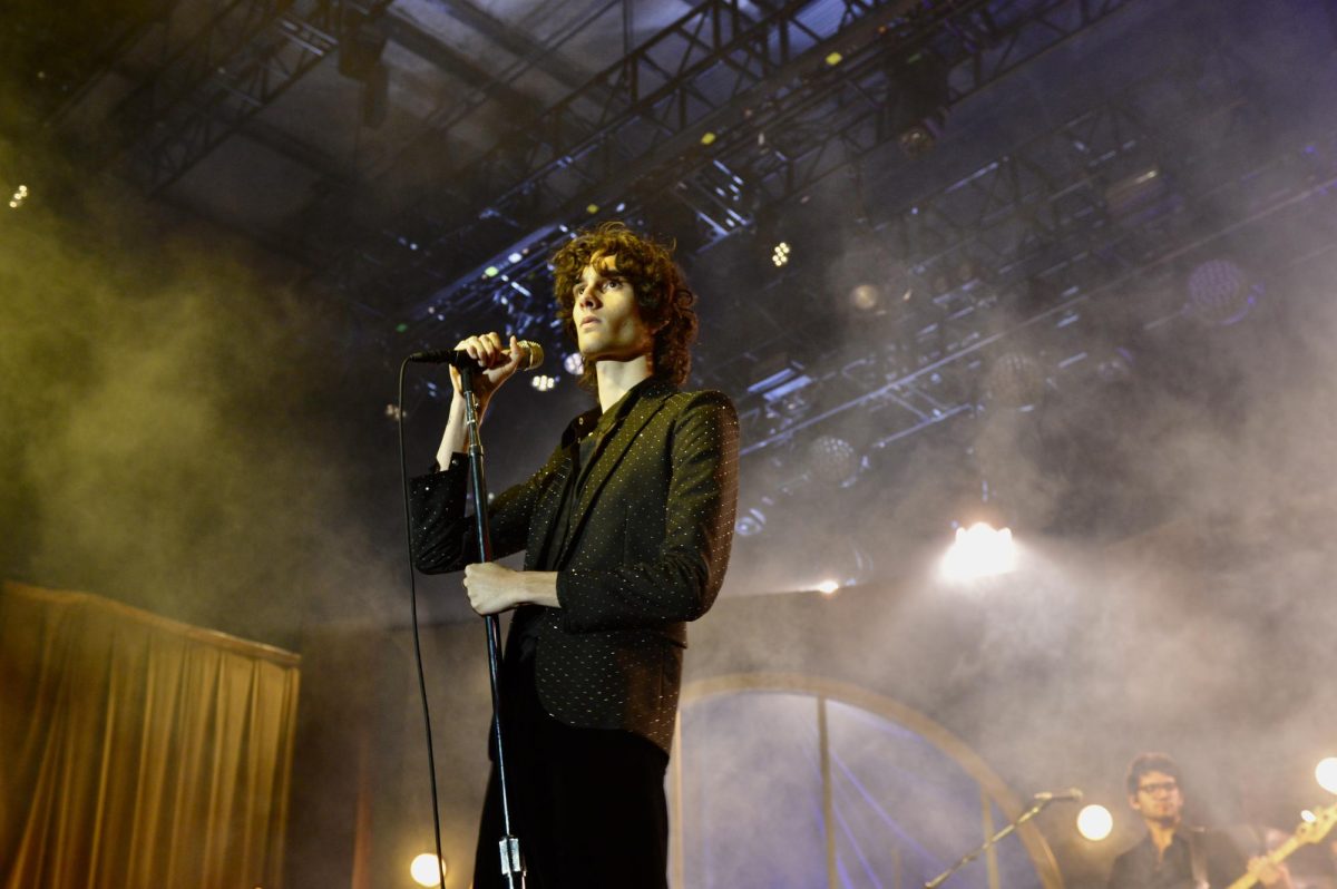 A man holds the microphone and looks into the crowd as fog surrounds him.