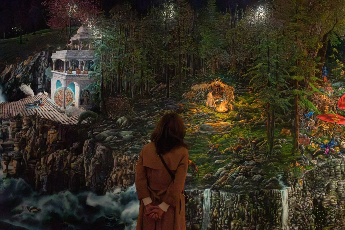 A person wearing a brown trench coat examines Raqib Shaw’s “Paradise Lost.”