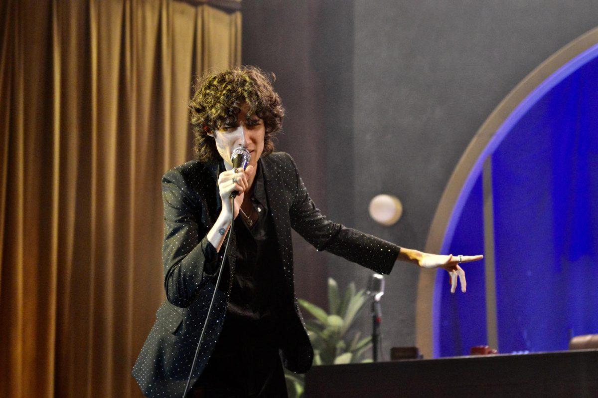 Singer holds microphone close to his mouth while he holds out his hand. 