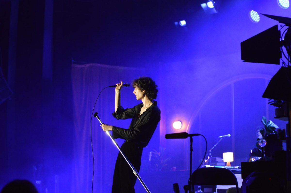 Singer in blue light bends a mic stand as he pulls a microphone to his mouth. 