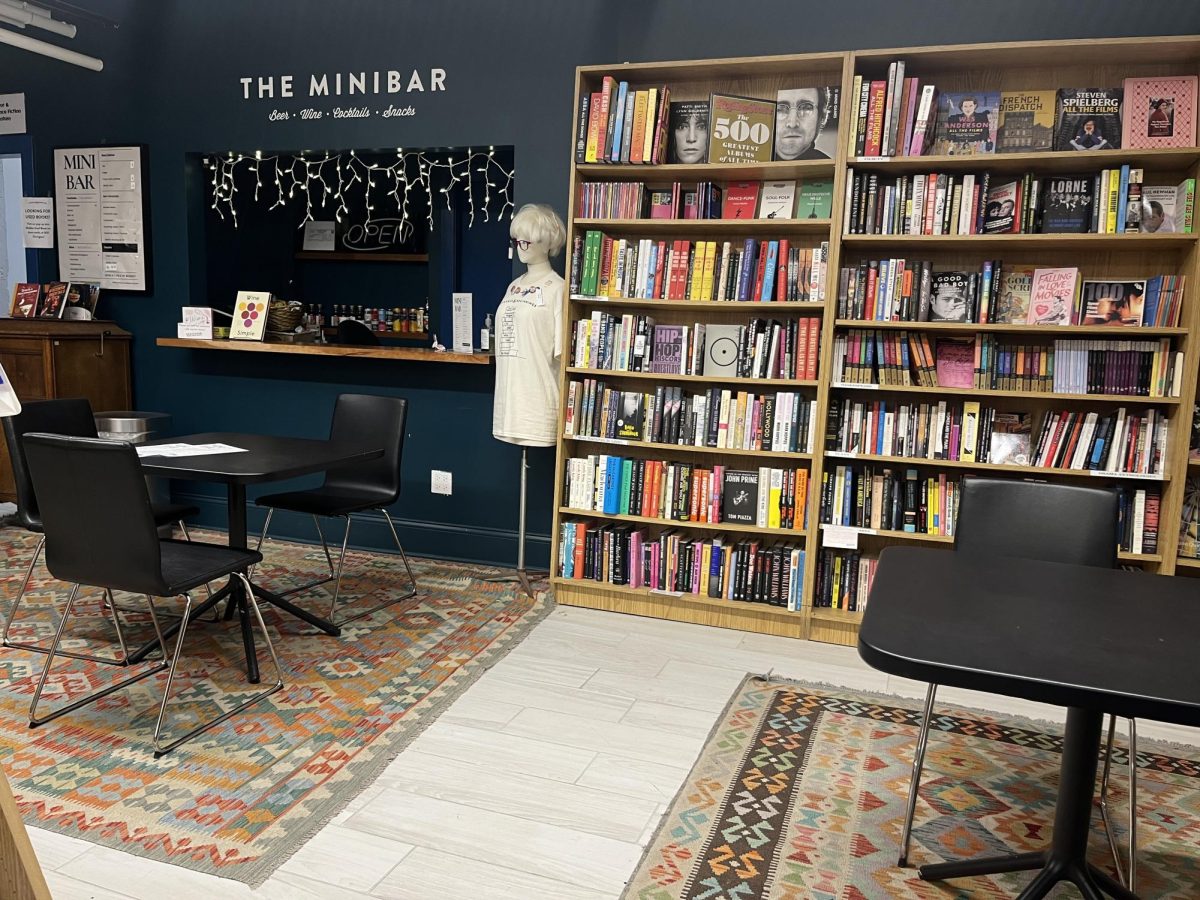 A mini bar with a table and chairs in front of it and bookshelves to the right with another table in front of them