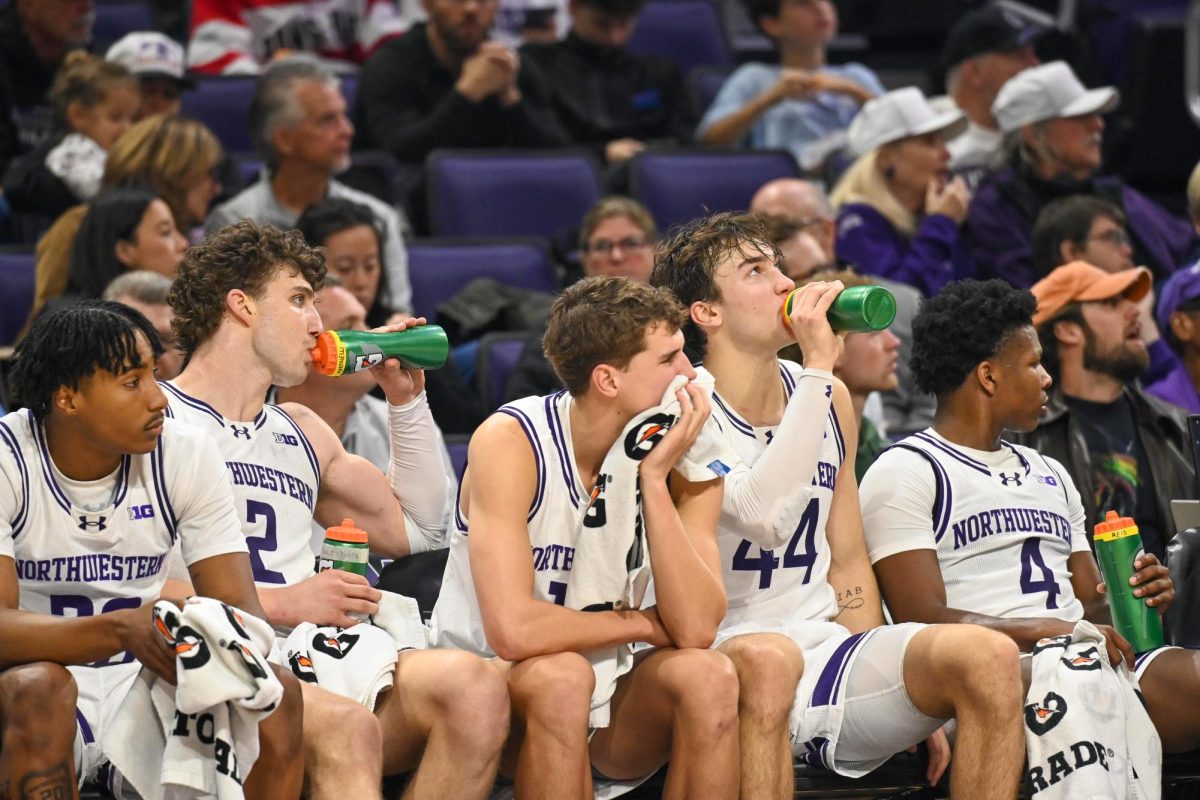 Basketball players sit on a sideline bench drinking water. 