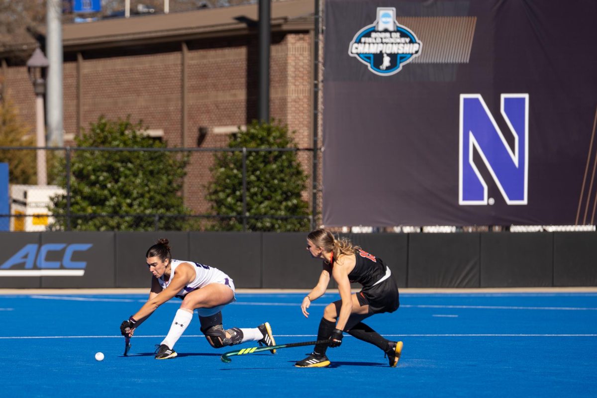 A player in a white jersey passes the ball while a player in a black jersey defends. 
