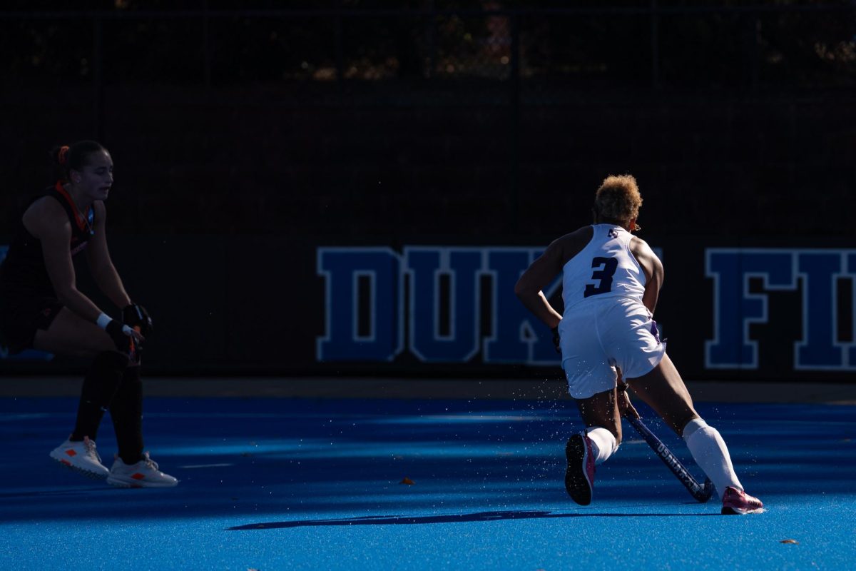A player in a white jersey runs with the ball as a player in a black jersey watches. 