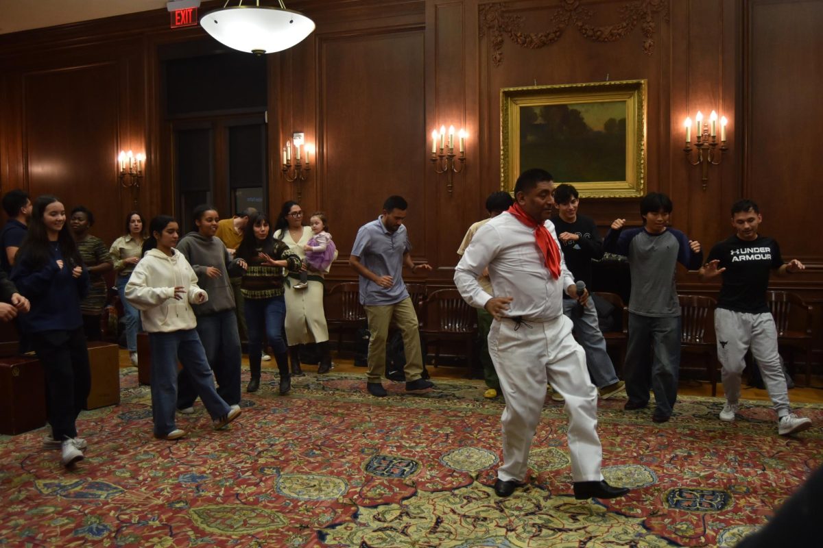 Person in white with red scarf leads people in a dance.