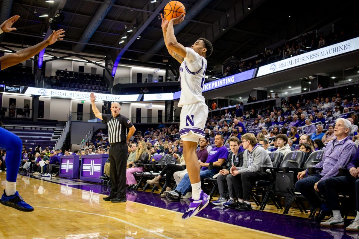 A player in a white jersey shoots a three-pointer from the corner in front of onlooking fans.