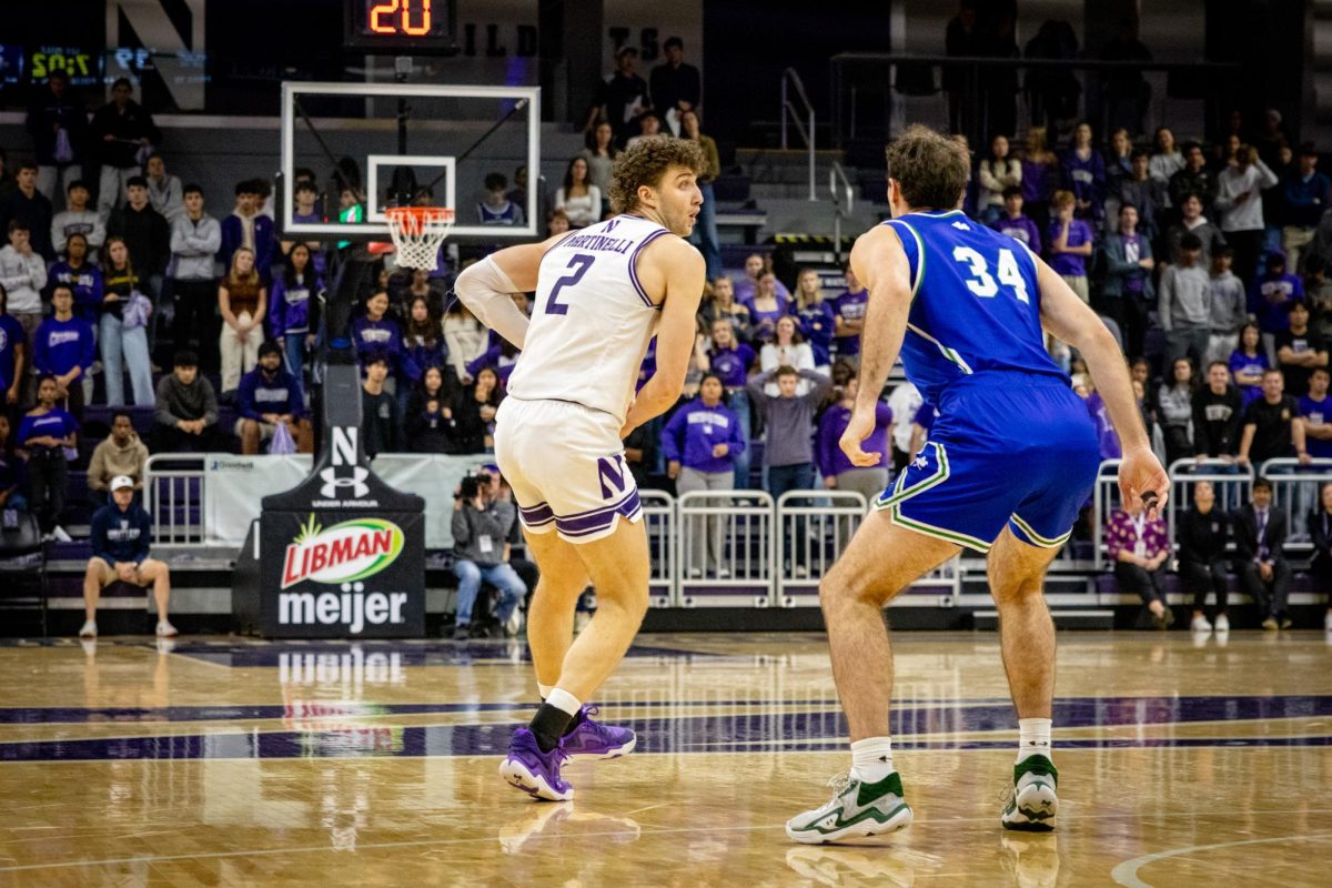 A player in a white jersey faces up towards the basket against an opponent in a blue jersey.