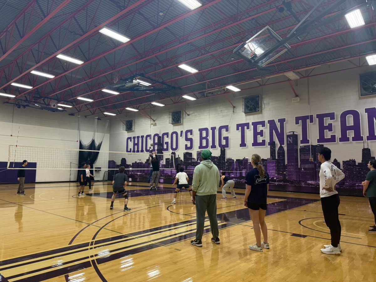 Northwestern students are divided into two sides by a volleyball net and are playing a volleyball game on a basketball court.