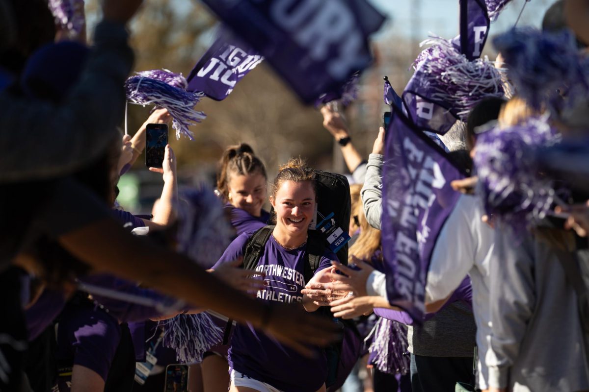 A player in purple smiles as she walks through a tunnel of flags and pom-poms. 