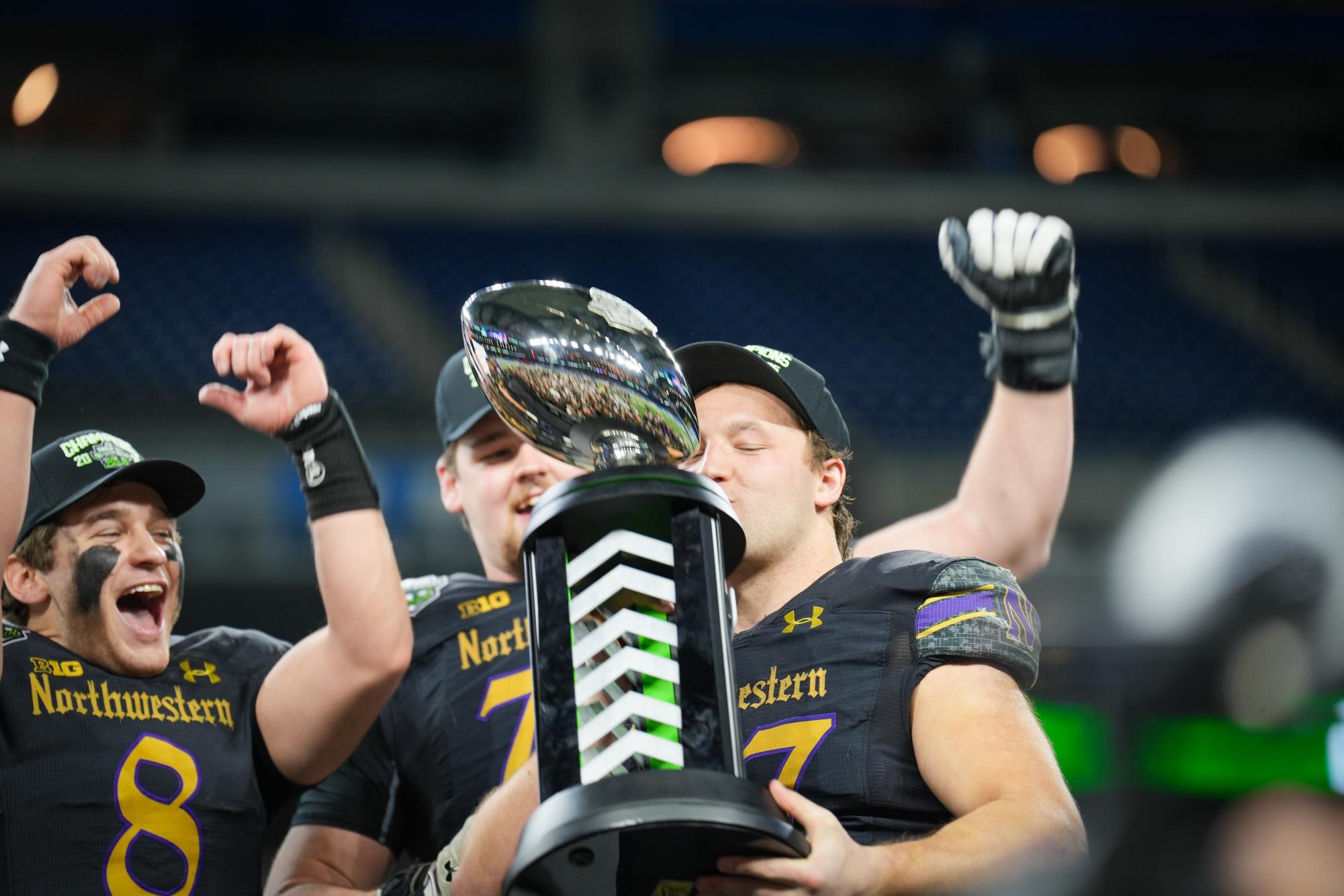 A player holds a trophy while others celebrate behind them.