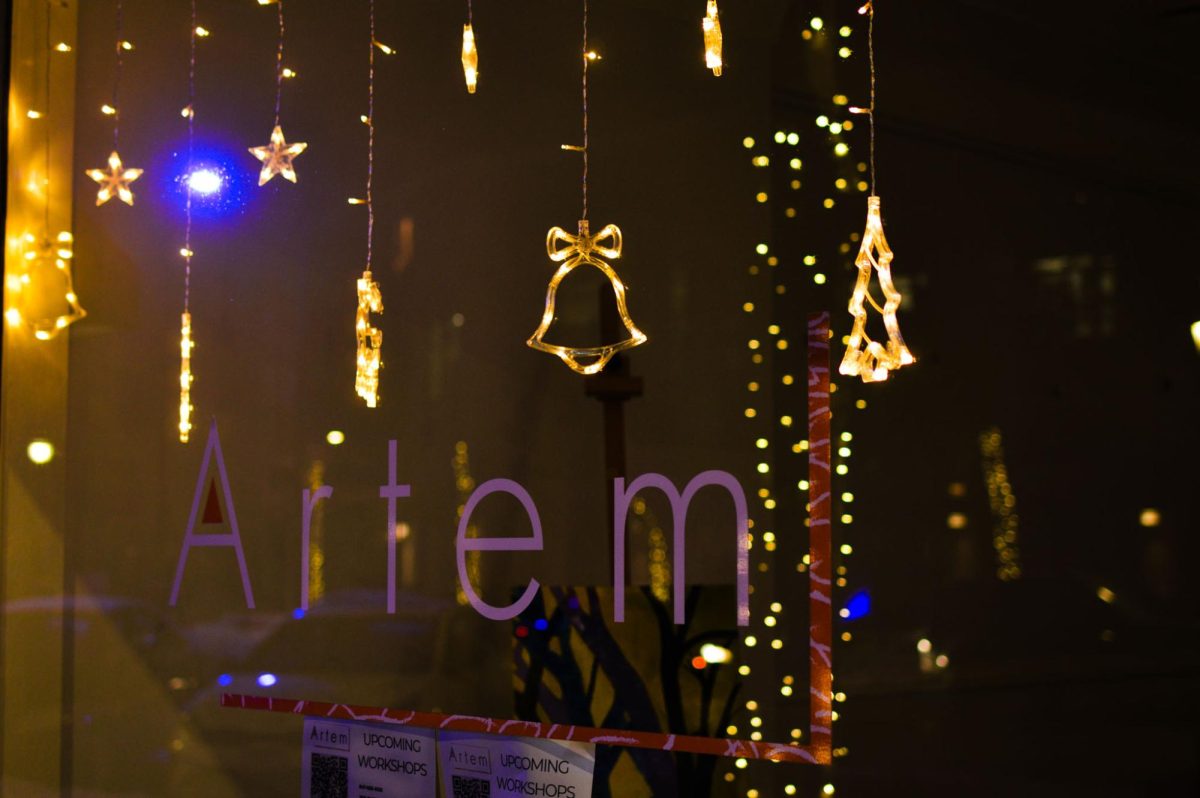 Small lights in the shape of Christmas trees, bells and gifts hang in a window.