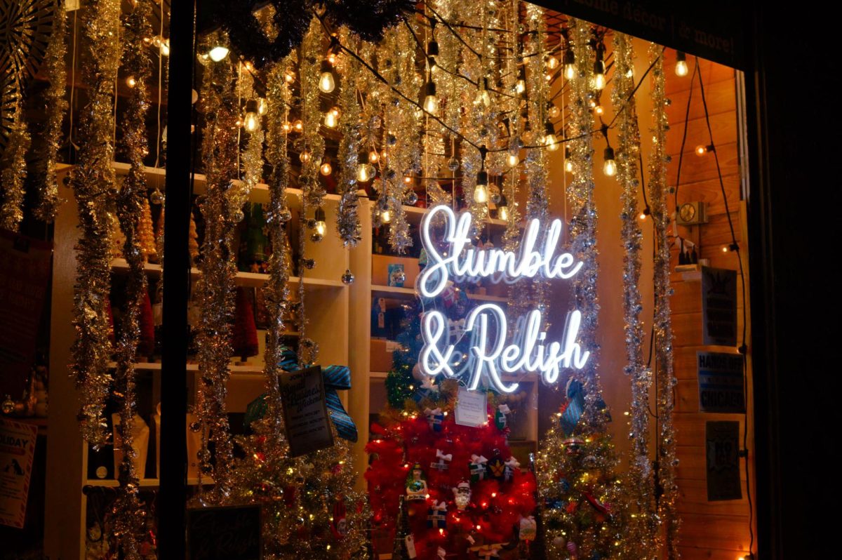 A glowing sign reads &ldquo;Stumble & Relish&rdquo; in front of hanging lights, ornaments and tinsel. 